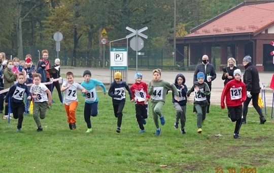 Na zdjęciu widać grupę dziesięciu chłopców rozpoczynających bieg. Na linii startu stoją trzy dorosłe osoby, z lewej kibice.