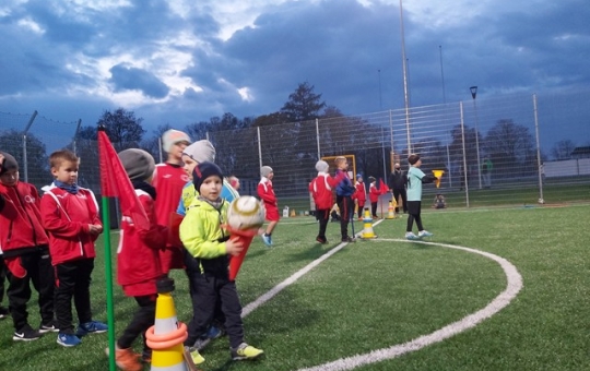 Na zdjęciu dwie dziecięce drużyny oczekują na rozpoczęcie konkurencji. Zdjęcie wykonane wieczorem, na oświetlonym boisku.