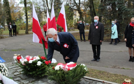 Na zdjęciu Burmistrz Miasta Hajnówka kładzie wieniec białoczerwonych kwiatów na pomniku. W tle widać delegację Rady Miasta Hajnówka oraz cztery polskie flagi.