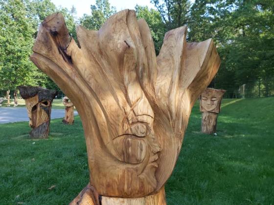 Fragment rzeźby wykonanej w drewnie stojącej na trawniku. W tle inne rzeźby i drzewa.