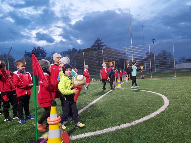 Na zdjęciu dwie dziecięce drużyny oczekują na rozpoczęcie konkurencji. Zdjęcie wykonane wieczorem, na oświetlonym boisku.