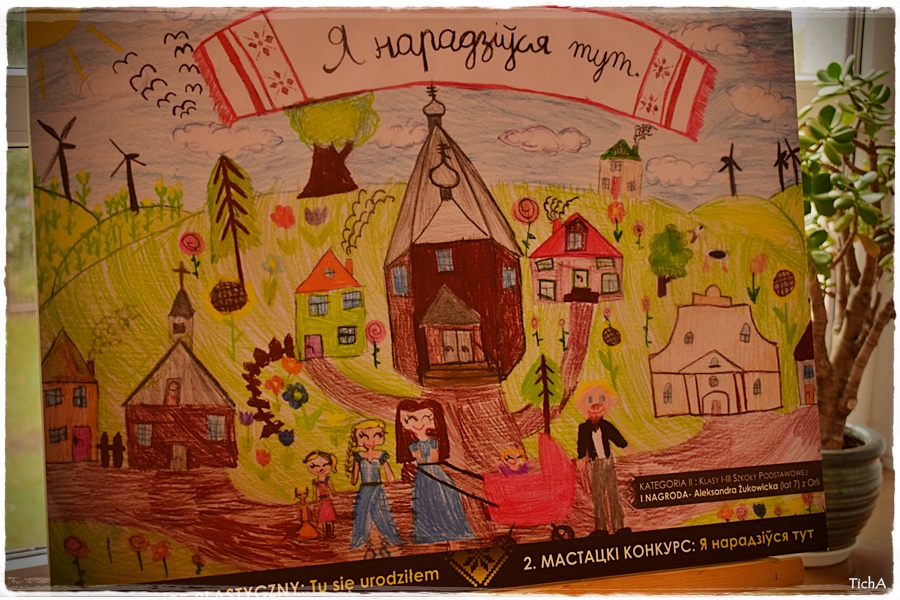 Zdjęcie przedstawia nagrodzoną pracę Aleksandry Żukowickiej-I miejsce w kategorii klasy I-III szkoły podstawowej. Na środku rysunku jest cerkiew, obok synagoga, kościół, domy, oraz na pierwszym planie rodzina. Nad nimi na ręczniku napis w języku białoruskim "Я нарадзіўся тут" co oznacza "Tu się urodziłem". 