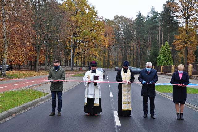 W poprzek ulicy stoją ustawieni w rzędzie , od lewej: Krzysztof Gawryluk, ksiądz Zygmunt Bronicki, ksiądz Jan Romańczuk, Jerzy Sirak, Walentyna Piertoczuk. Przecinają biało-czerwoną wstęgę rozpostartą w poprzek ulicy.