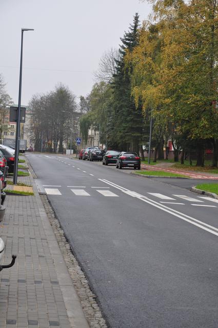 Zdjęcie przedstawia ulicę, przy której po obu stronach stoją zaparkowane samochody.
