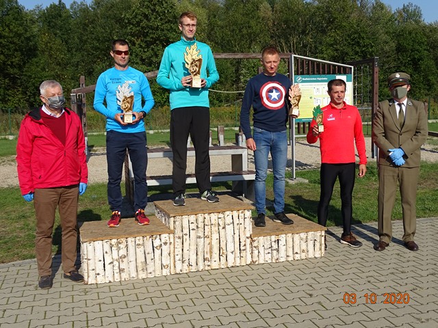 Zwycięzcy w kategorii Open Mężczyzn stoją na drewnianym podium. Z lewej strony towarzyszy im burmistrz. 